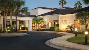 Un hotel moderno con un camino curvo, palmeras y una entrada bien iluminada.