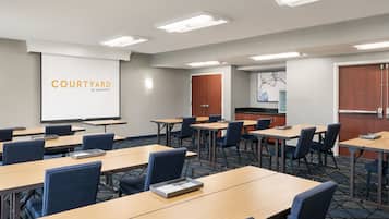 A conference room with multiple tables and chairs, a projection screen, and a kitchenette area.