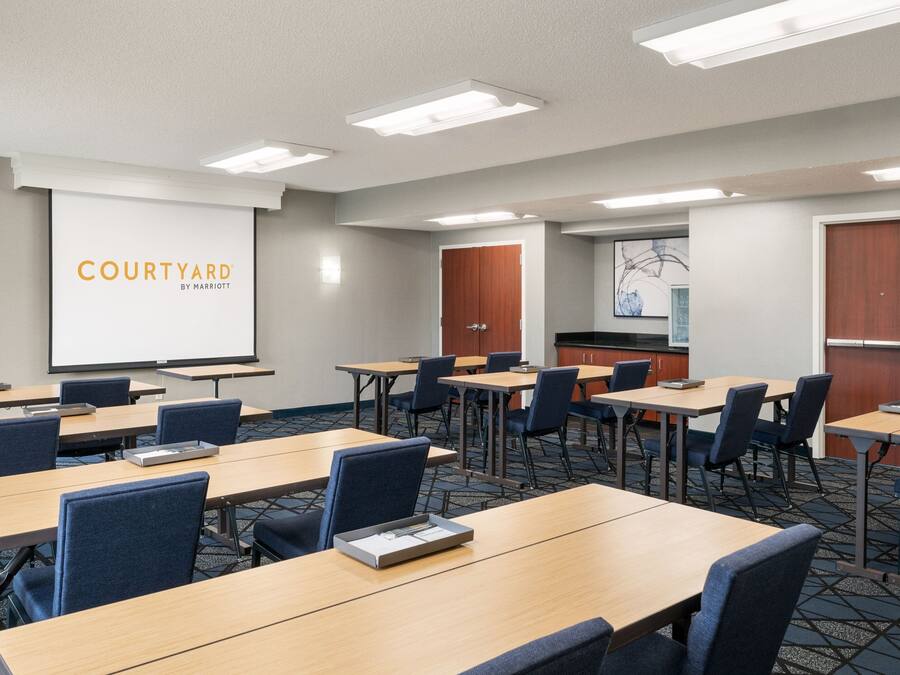 A conference room with multiple tables and chairs, a projection screen, and a kitchenette area.