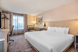 A hotel room with a large bed, a desk, a chair, a sofa, a lamp, and a painting on the wall.