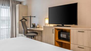 Una habitación de hotel con cama, escritorio, silla, televisor, microondas y armario.