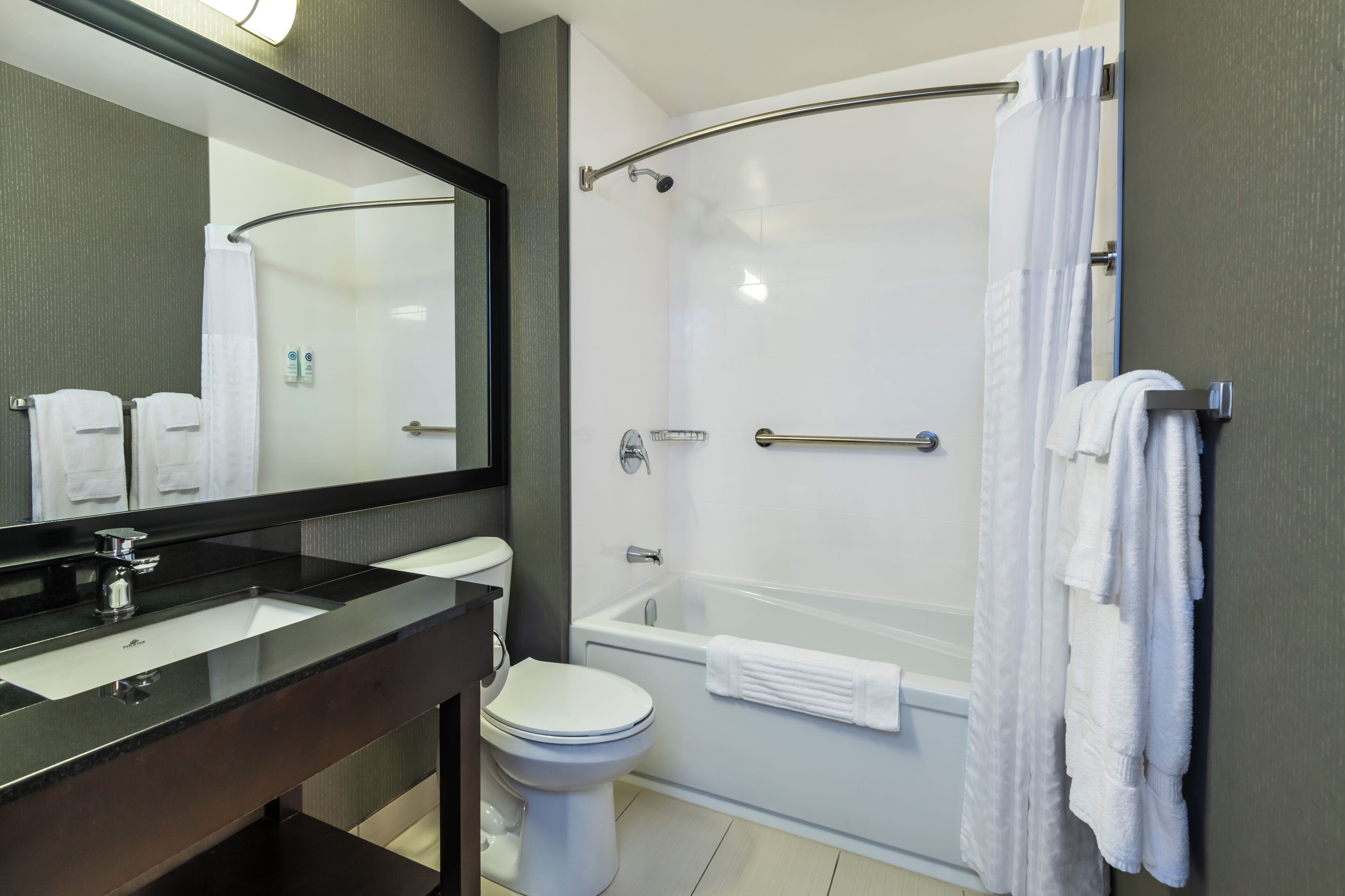 Un baño moderno con lavamanos de superficie negra, inodoro blanco, ducha con cerramiento de vidrio y un espejo grande.