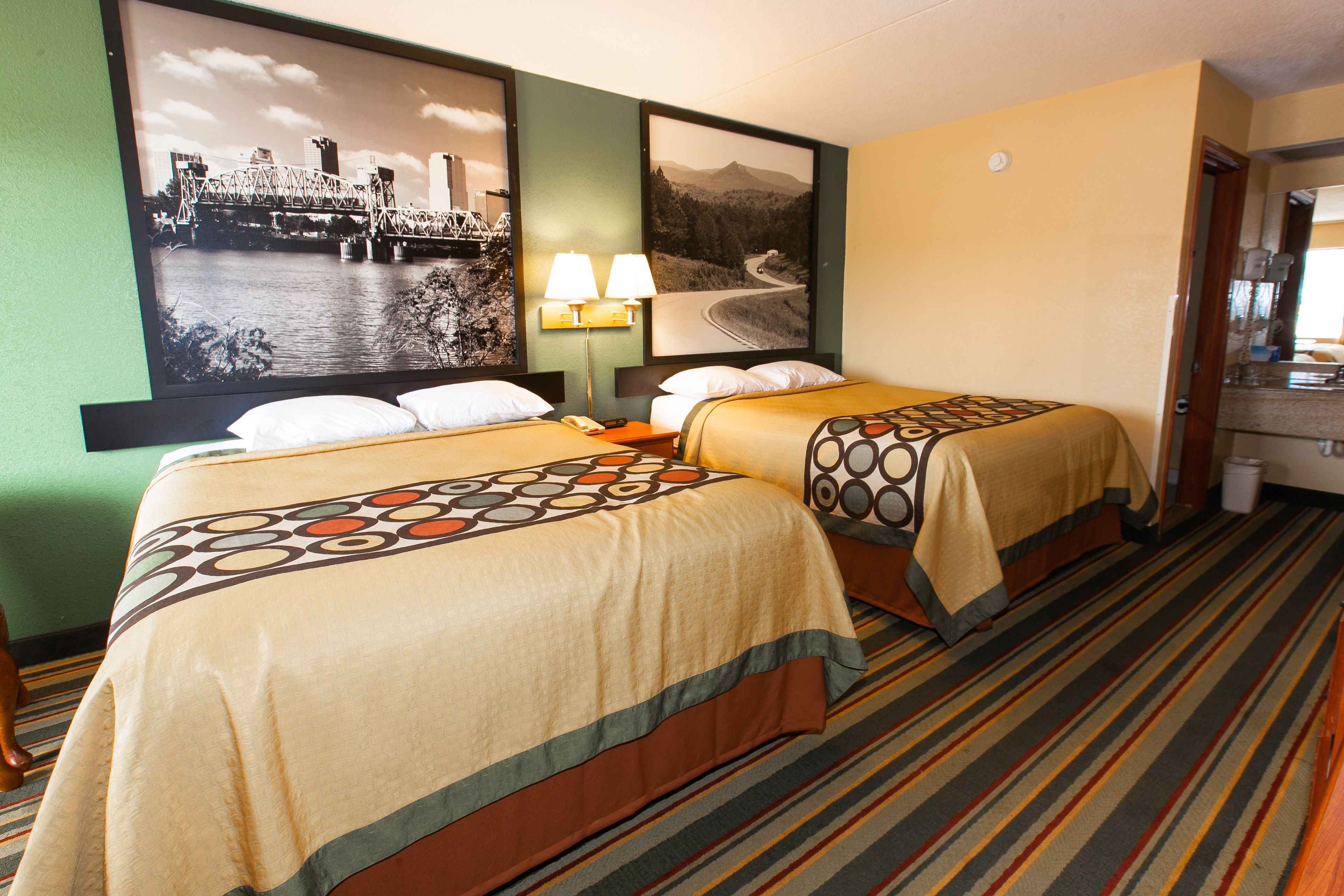 A hotel room with two beds, a nightstand, a lamp, and a large framed picture of a bridge.