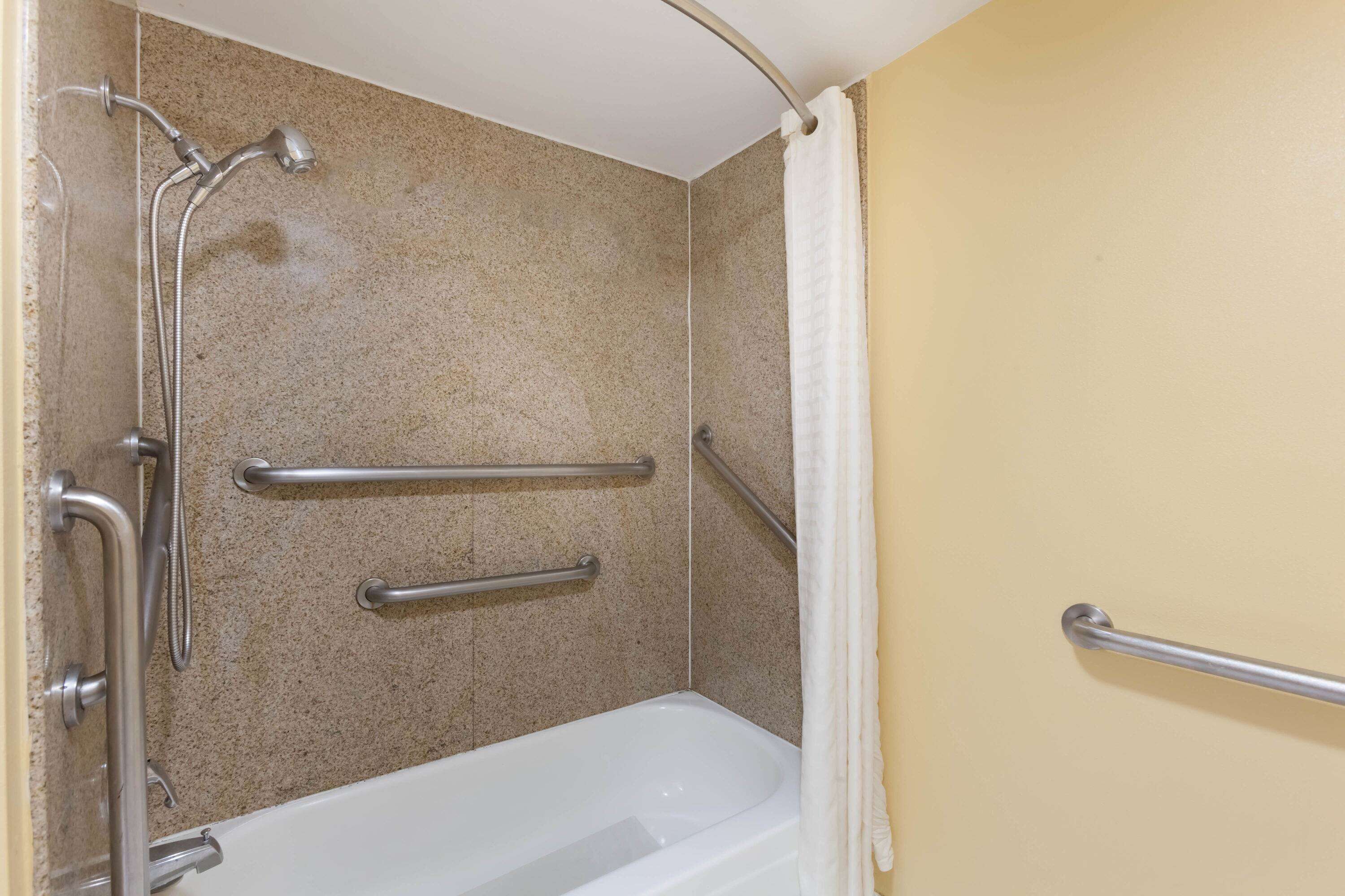 Ein Badezimmer mit Badewanne, Haltegriffen und Duschkopf.