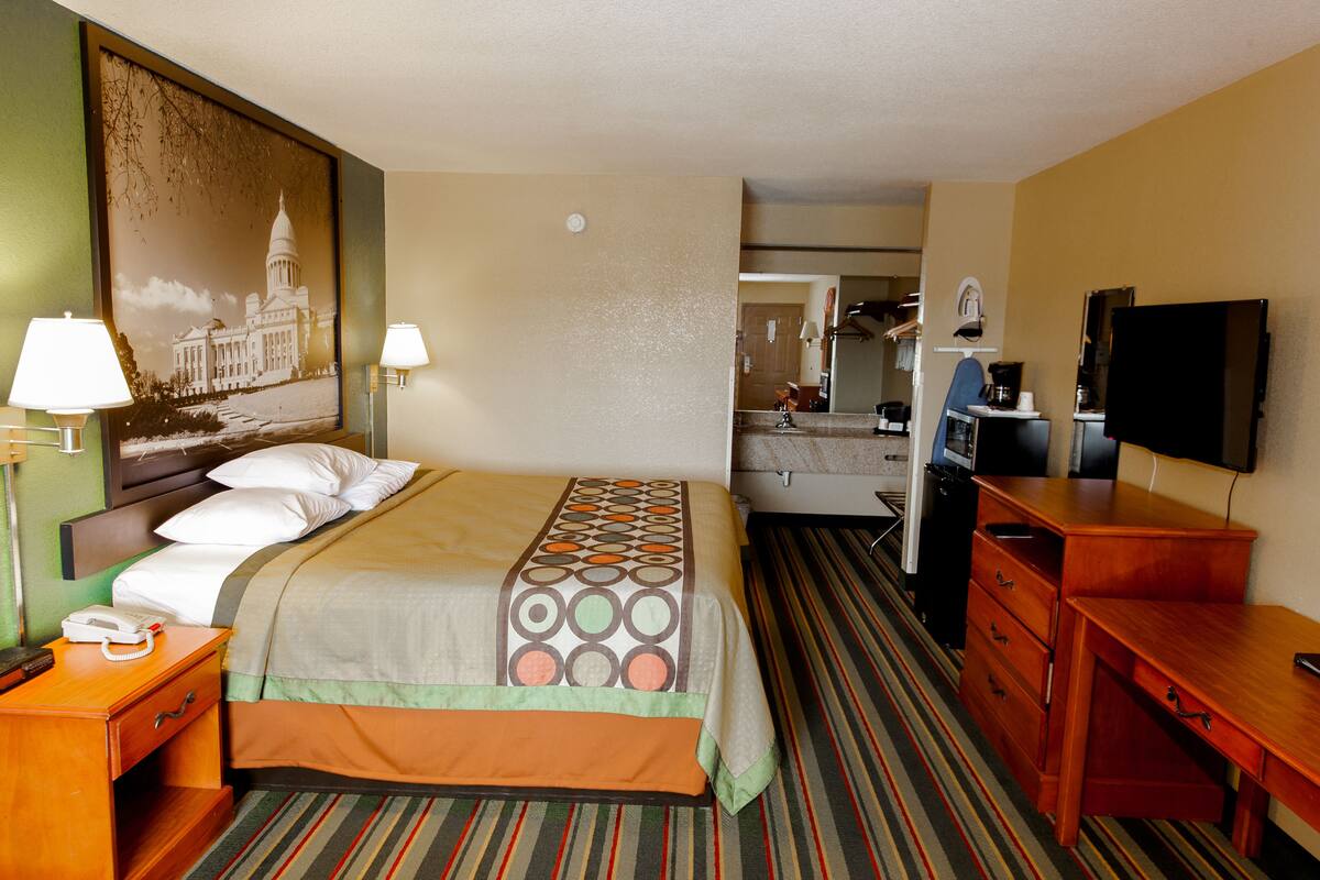 Ein Hotelzimmer mit Bett, Schreibtisch, Stuhl, Fernseher und einem Bild eines Gebäudes.