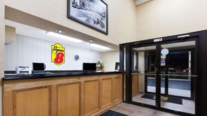 A hotel reception area with a wooden counter, a Super 8 logo, a clock, and a door leading outside. - Super 8 by Wyndham Jacksonville AR (Jacksonville)