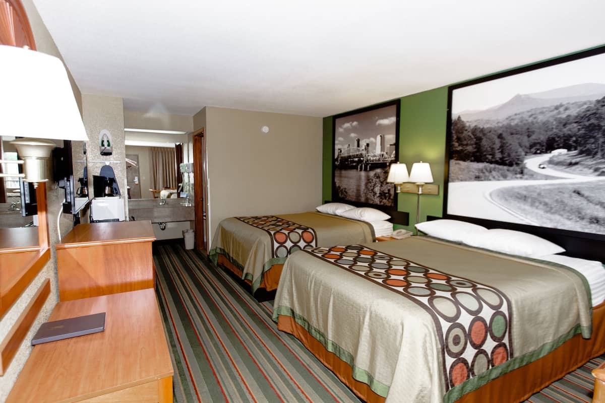 Ein Hotelzimmer mit zwei Betten, einem Schreibtisch, einem Stuhl, einer Lampe und einem großen Fenster mit Blick auf eine Landschaft.