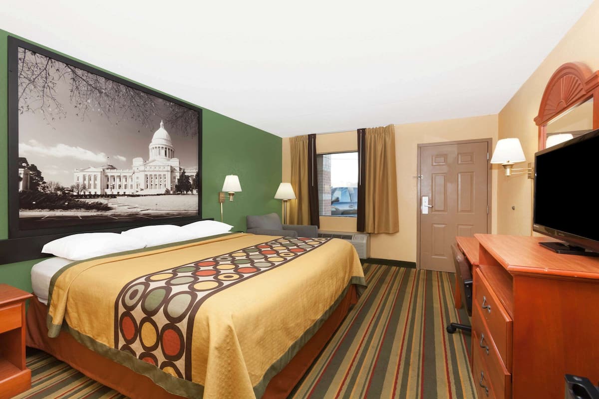 Ein Hotelzimmer mit einem großen Bett, einem Schreibtisch, einem Fernseher und einem an der Wand hängenden Bild eines Regierungsgebäudes.