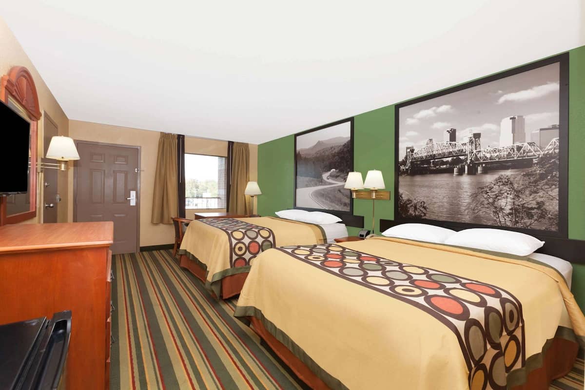 Ein Hotelzimmer mit zwei Betten, einem Schreibtisch, einem Fernseher und einem großen Stadtbild an der Wand.