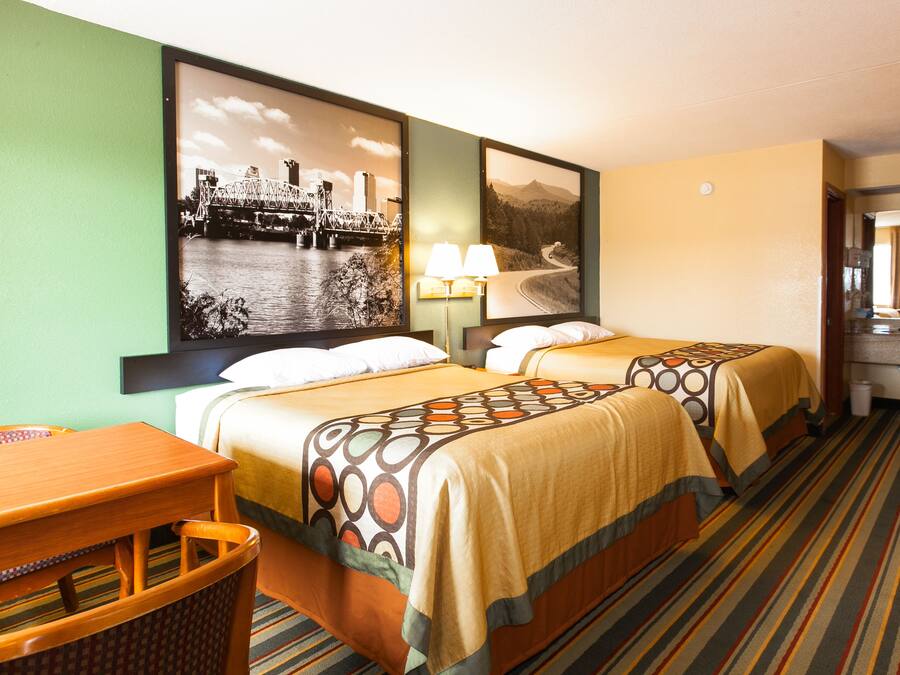 Une chambre d’hôtel avec deux lits, un bureau, une chaise, une télévision et des œuvres d’art accrochées aux murs.