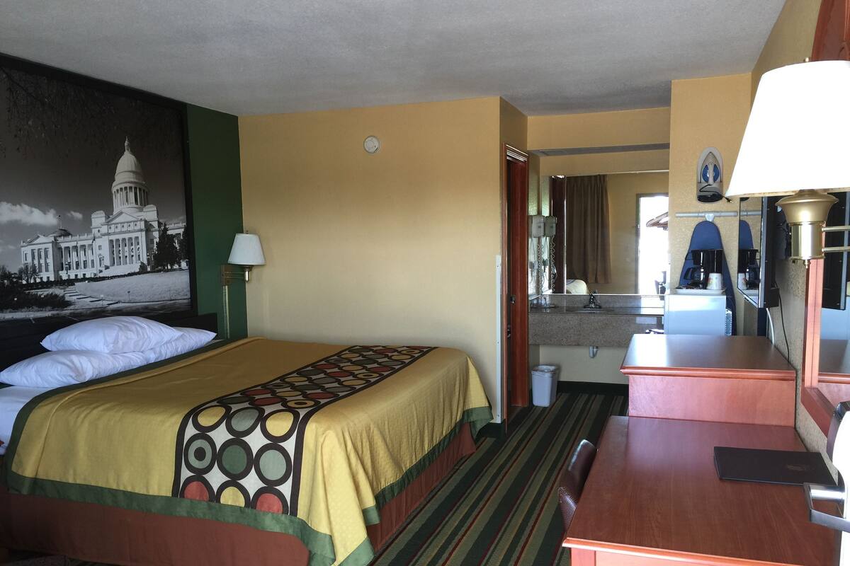 Ein Hotelzimmer mit Bett, Schreibtisch, Spiegel, Bad und Blick auf ein Gebäude.