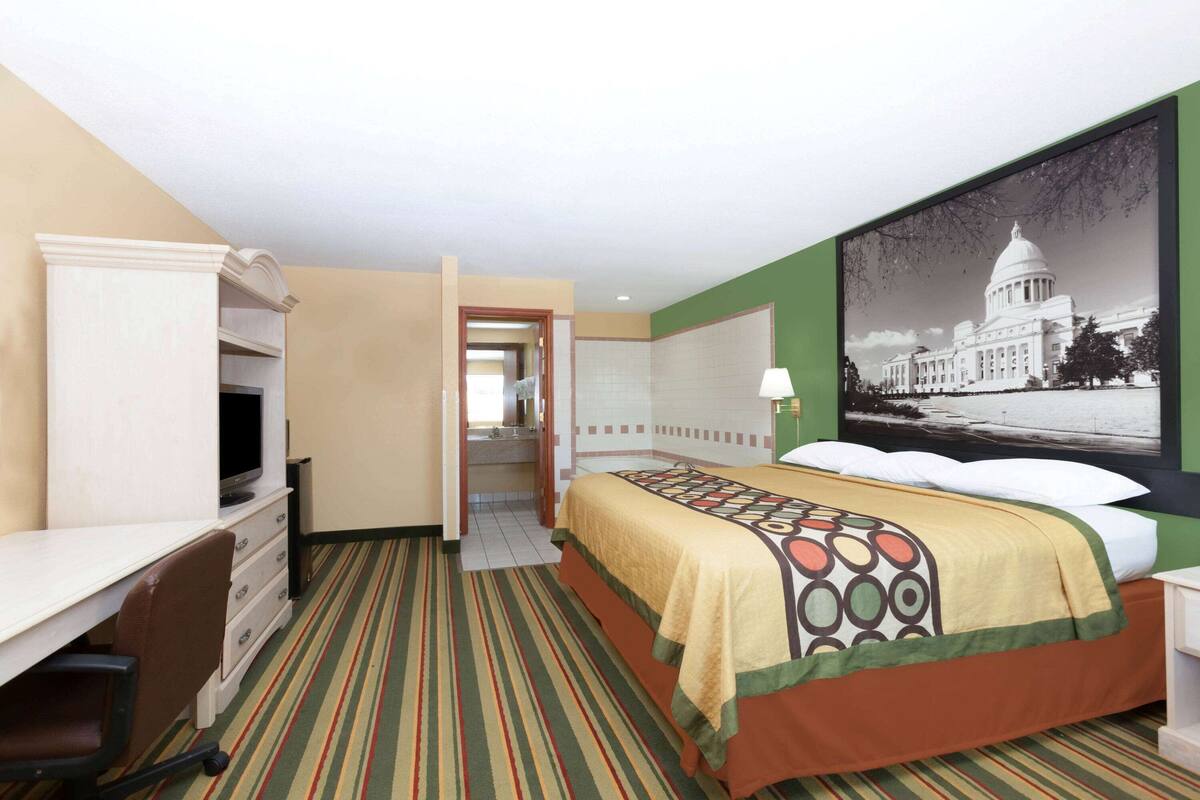 Ein Hotelzimmer mit Bett, Schreibtisch, Stuhl und einem großen Wandbild eines Regierungsgebäudes.