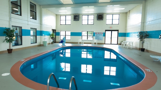 An indoor swimming pool with clear pool rules posted, surrounded by windows and potted plants. - Super 8 by Wyndham Jacksonville AR (Jacksonville)