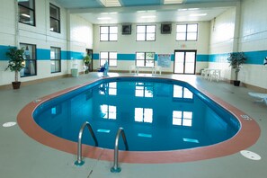 Una piscina interior con normas claras exhibidas, rodeada de ventanas y plantas en macetas.