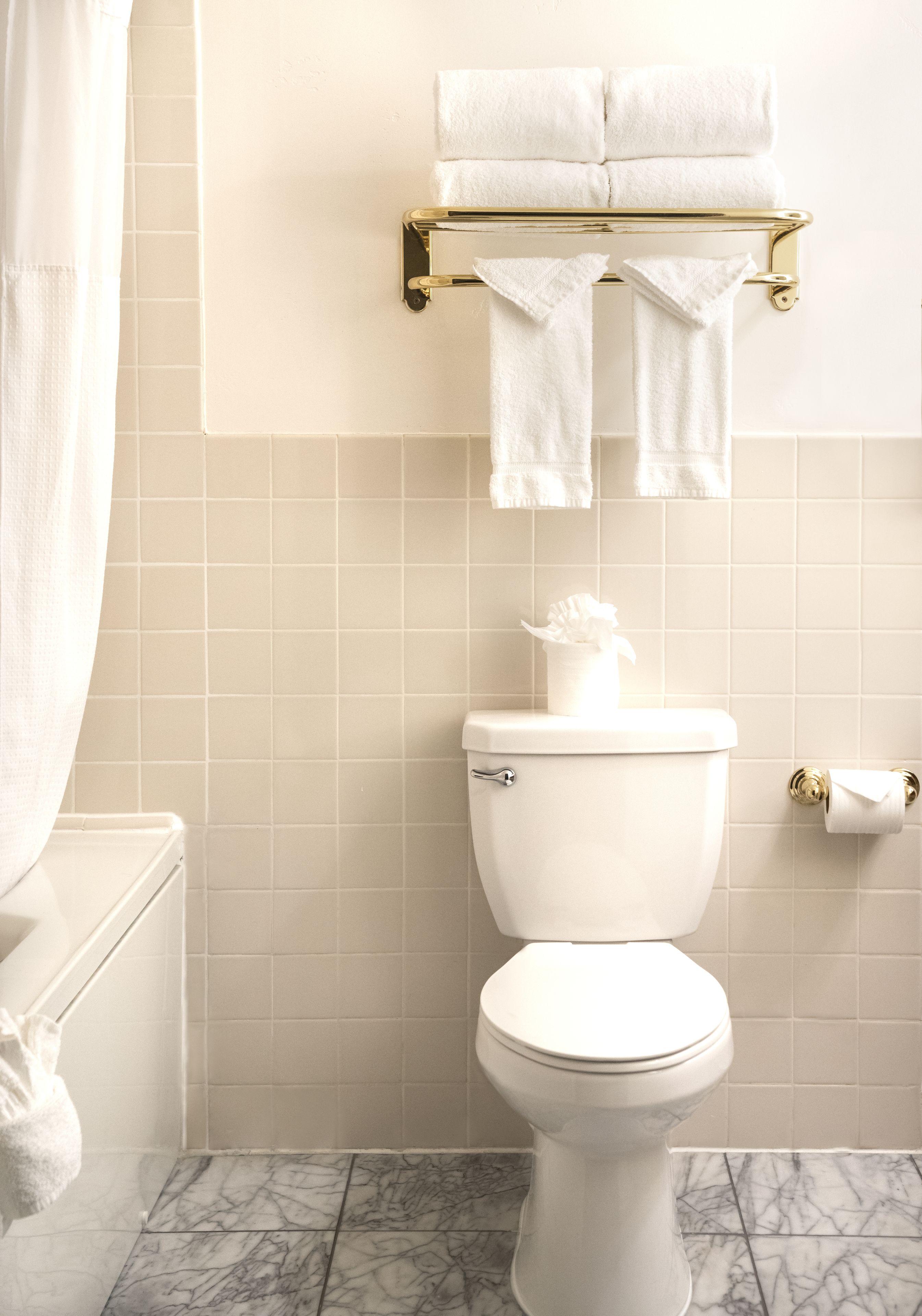 Une salle de bain équipée de toilettes, d’un porte-serviettes avec des serviettes, d’un support à papier toilette et d’un sol carrelé en marbre.