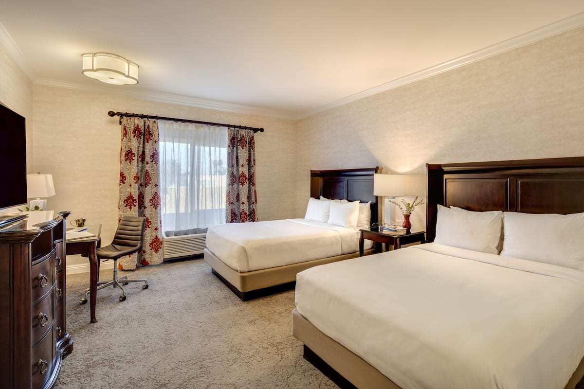 A hotel room with two beds, a desk, a chair, a TV, and a window with curtains.