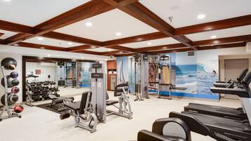 A gym with treadmills, weight machines, and a wall mural of a beach scene.