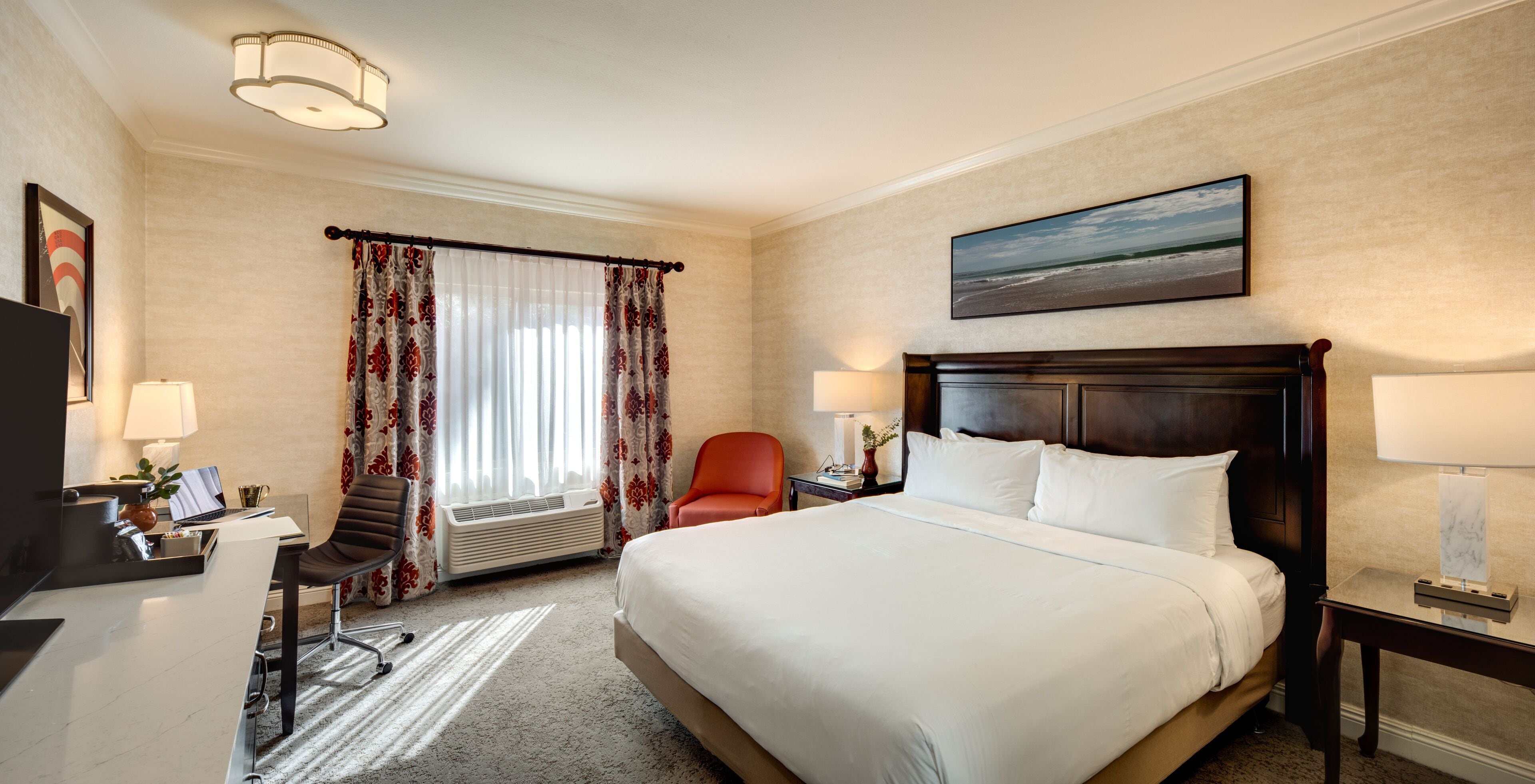 A hotel room with a large bed, a desk with a chair, a TV, and a painting on the wall.