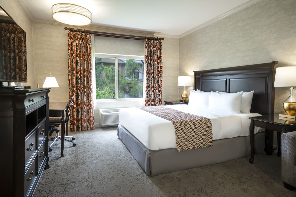 A hotel room with a large bed, two bedside tables with lamps, a dresser, and a window with curtains.