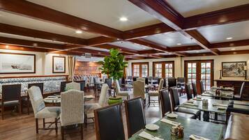 A restaurant with wooden beams, patterned wallpaper, and a variety of seating including booths and tables.