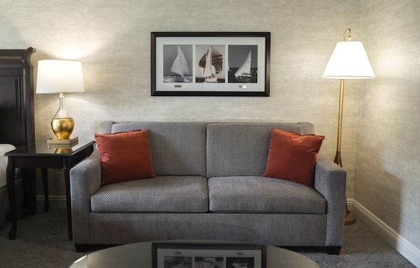 A grey sofa with red cushions, a framed picture of sailboats on the wall, a gold lamp on a side table, and a floor lamp.
