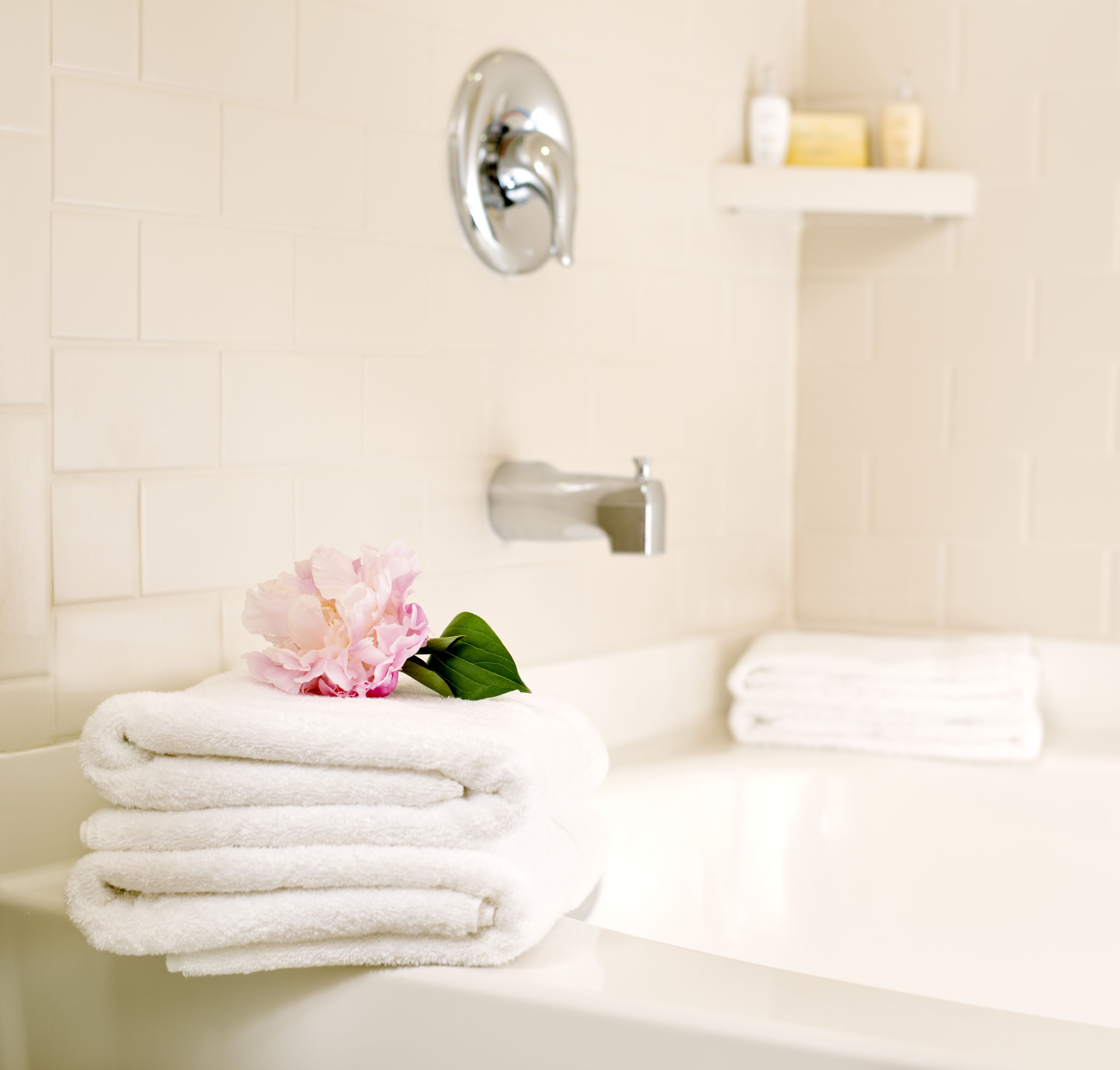 A bathroom with a white bathtub, a stack of white towels, and a pink flower on the edge.