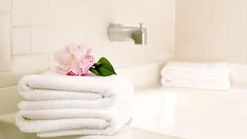 A bathroom with a white bathtub, a stack of white towels, and a pink flower on the edge.
