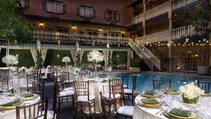 A formal outdoor dining area with multiple tables set for a meal, surrounded by a pool and a multi-level building with balconies.