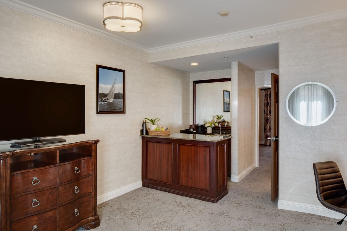 A hotel room with a wooden dresser, a flat-screen TV, a large mirror, and a round mirror.
