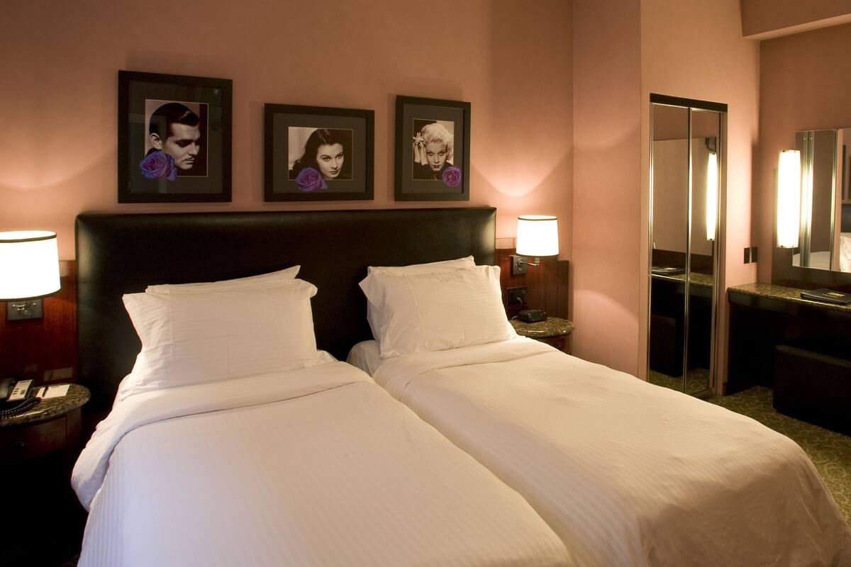 A hotel room with a double bed, two bedside tables with lamps, a large mirror, and three framed pictures on the wall.