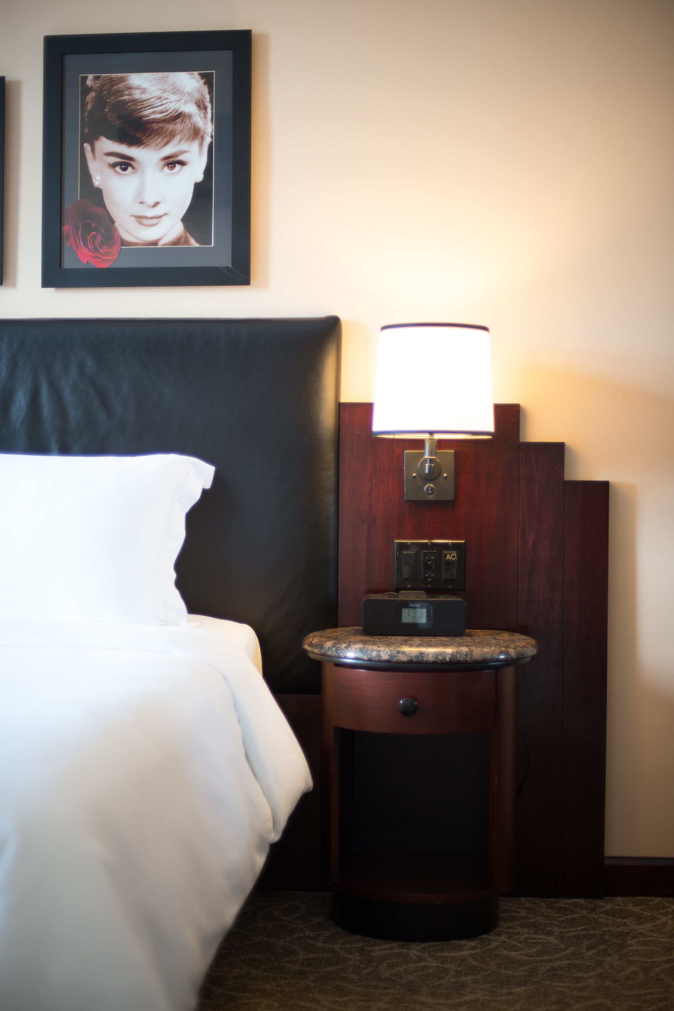 Ein Hotelzimmer mit einem Bett, einem Nachttisch mit Lampe und einem gerahmten Bild an der Wand.
