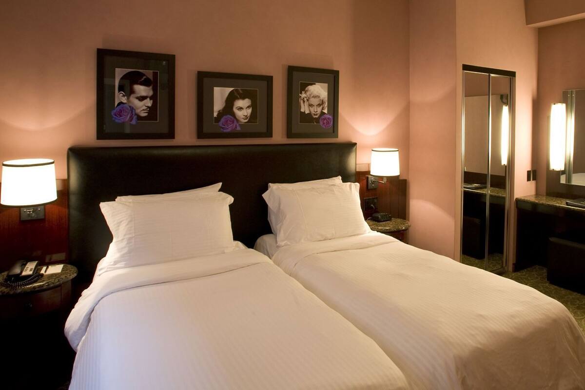 A hotel room with a double bed, bedside lamps, a mirror, and framed pictures on the wall.