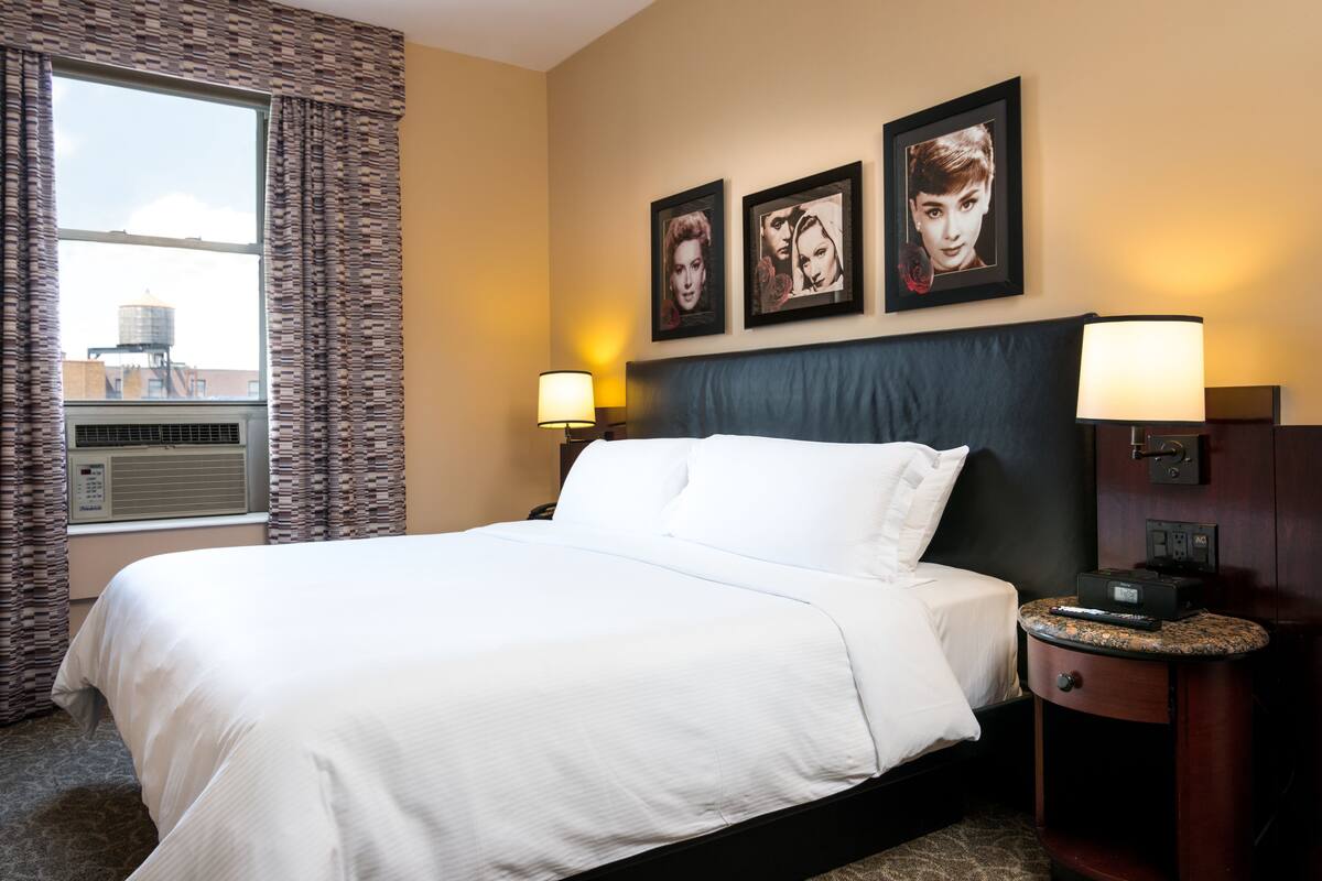 A hotel room with a large bed, two bedside lamps, a headboard, and three framed pictures on the wall.