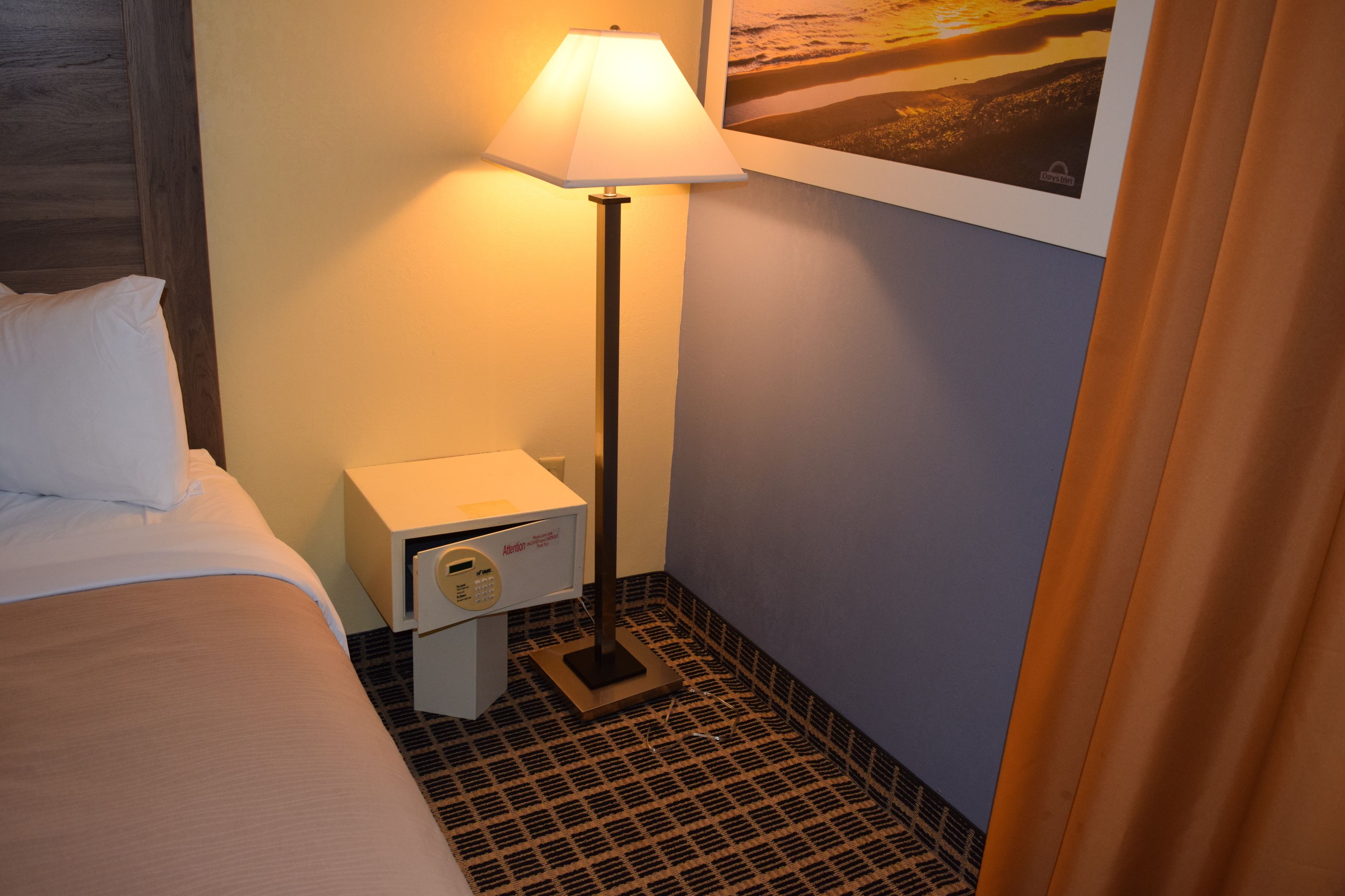 A hotel room with a bed, a nightstand with a lamp, a microwave, and a framed picture on the wall.