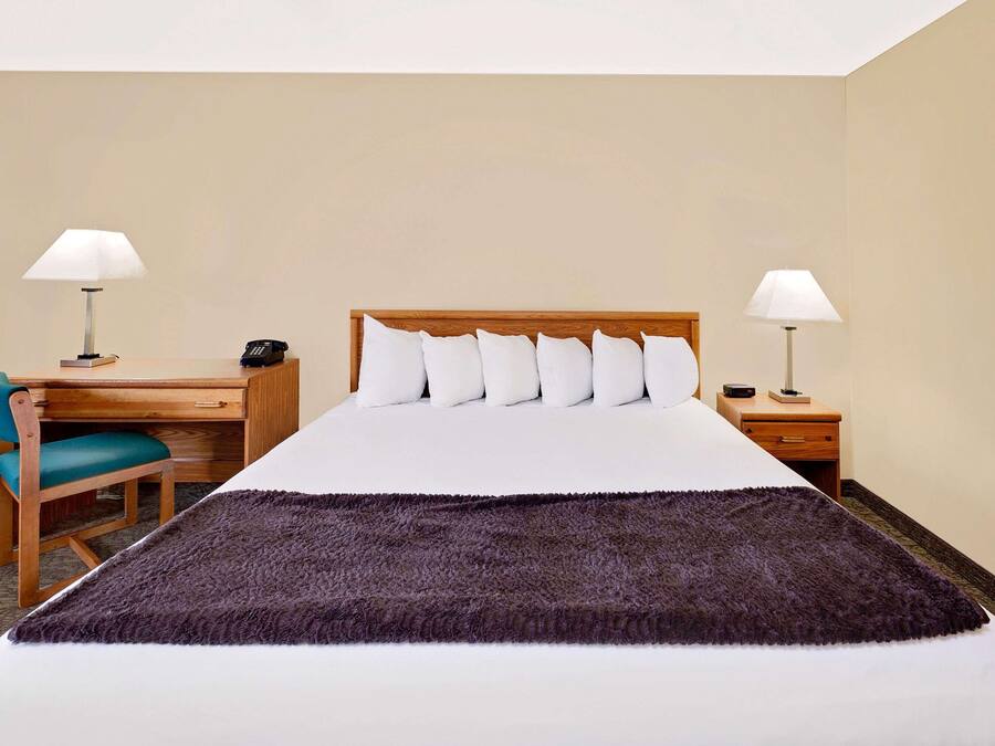 A hotel room with a bed, two bedside tables, a desk with a chair, and two lamps.