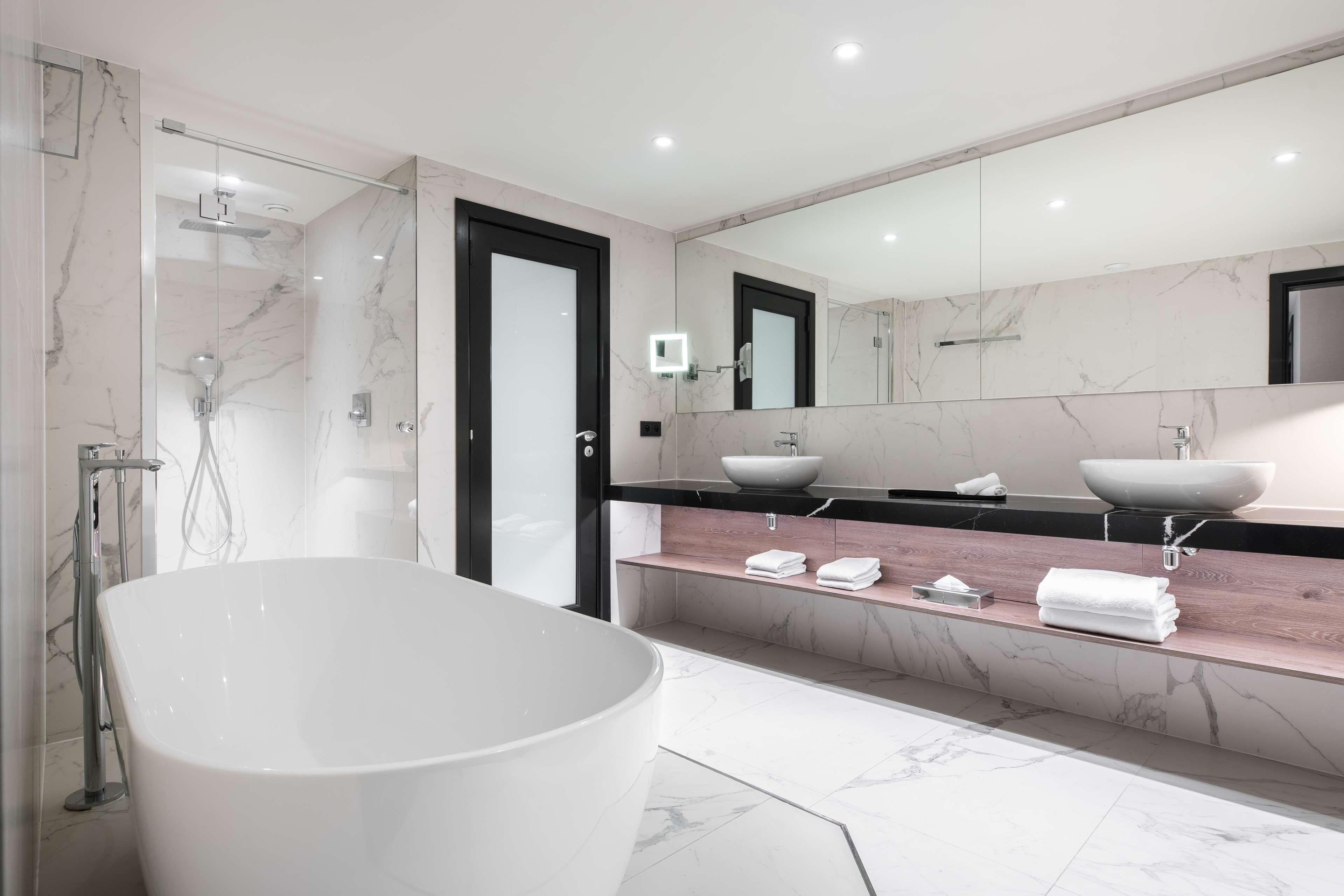 Een moderne badkamer met een vrijstaand bad, een douche met glazen wanden en een wastafelmeubel met een marmeren blad en twee wasbakken.