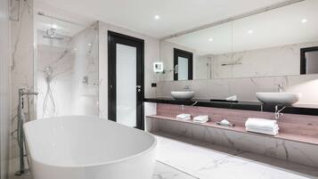 Een moderne badkamer met een vrijstaand bad, een douche met glazen wanden en een wastafelmeubel met een marmeren blad en twee wasbakken.
