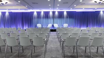 Ein Konferenzraum mit Reihen weißer Stühle, einem Teppichboden und einer blauen Vorhangwand.