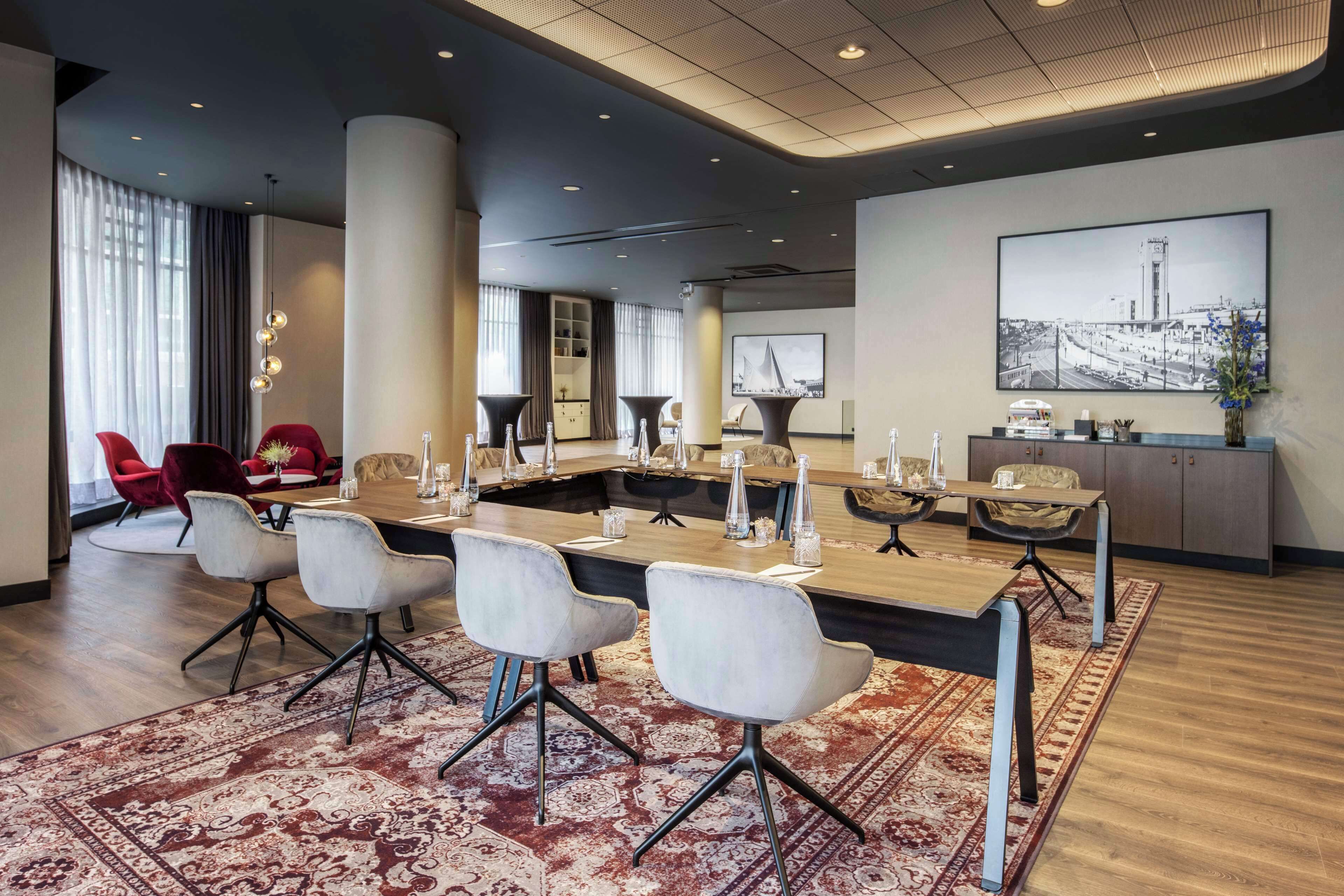 A modern conference room with a long table, white chairs, and a patterned rug.