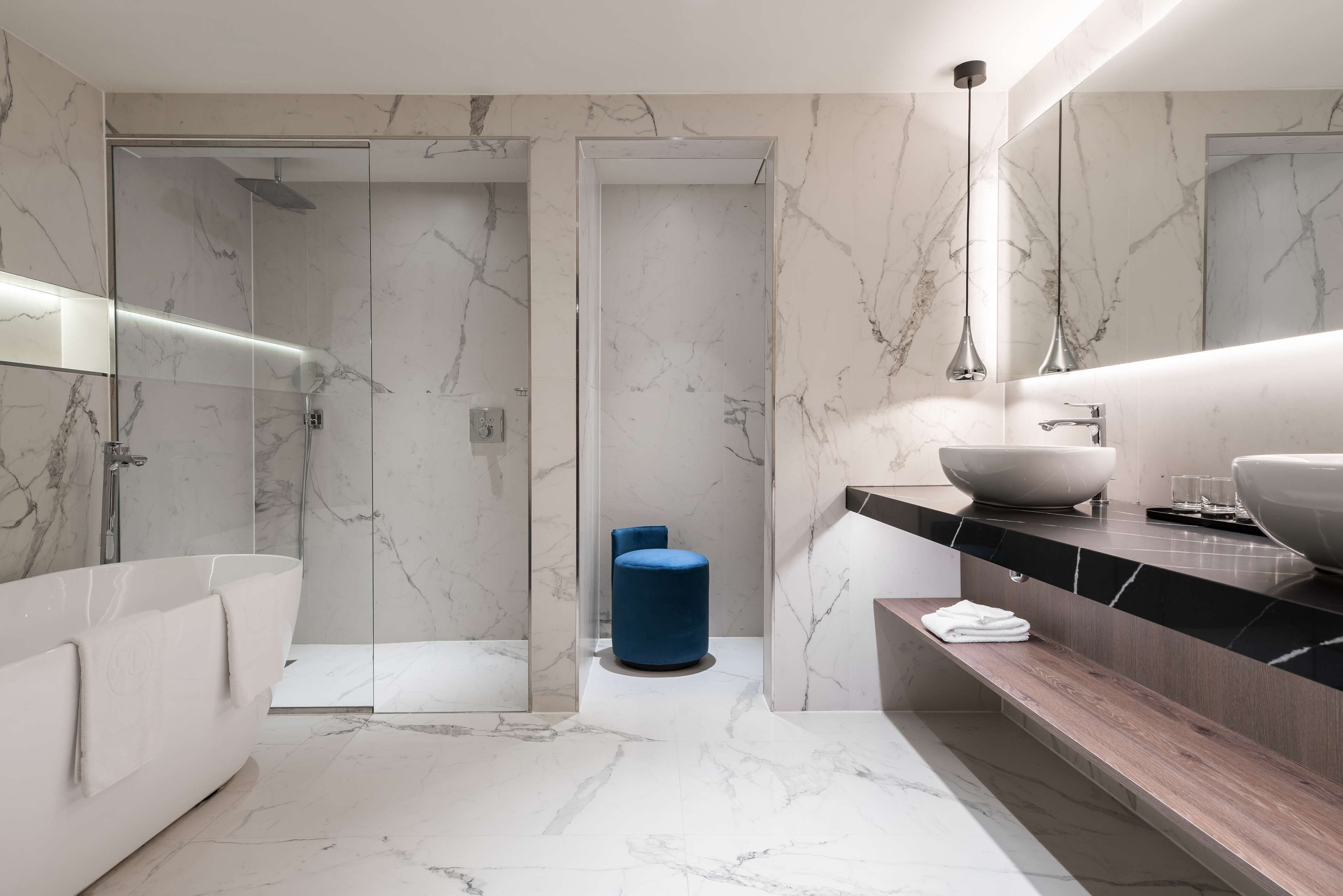 Een moderne badkamer met een douchecabine van glas, een groot wit bad en een houten wastafelmeubel met een ruime wastafel en twee wasbakken.