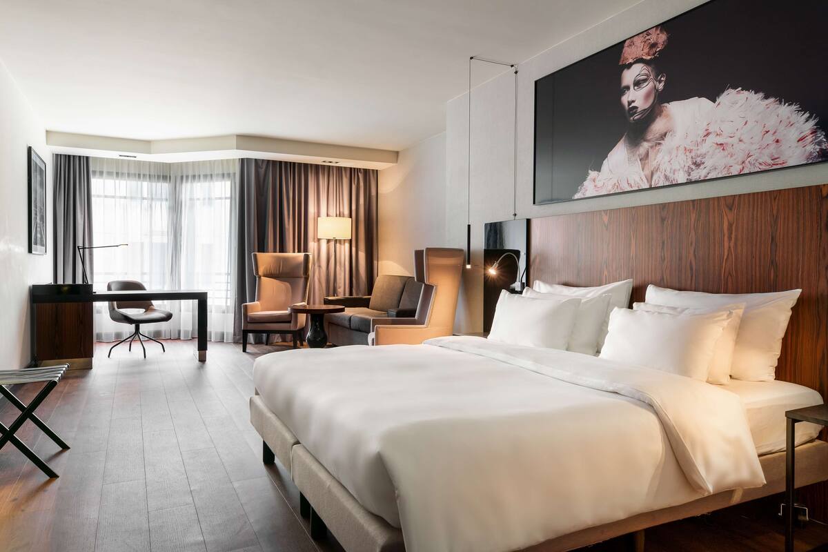 Une chambre d’hôtel avec un grand lit, un bureau, une chaise et un grand tableau au mur.