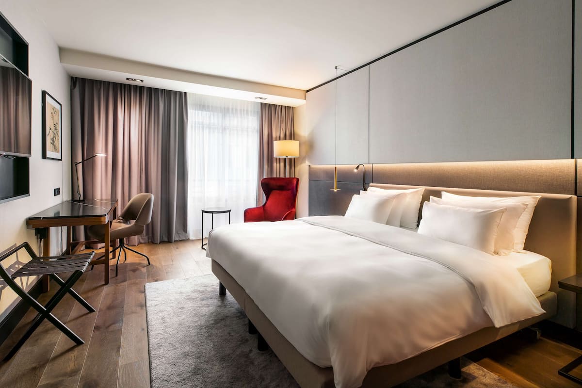 Une chambre d’hôtel avec un grand lit, un bureau, une chaise rouge et une lampe.