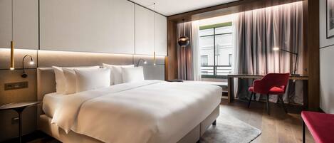 Habitación de hotel moderna con una cama grande, un escritorio, una silla y vistas de la ciudad a través de amplias ventanas.