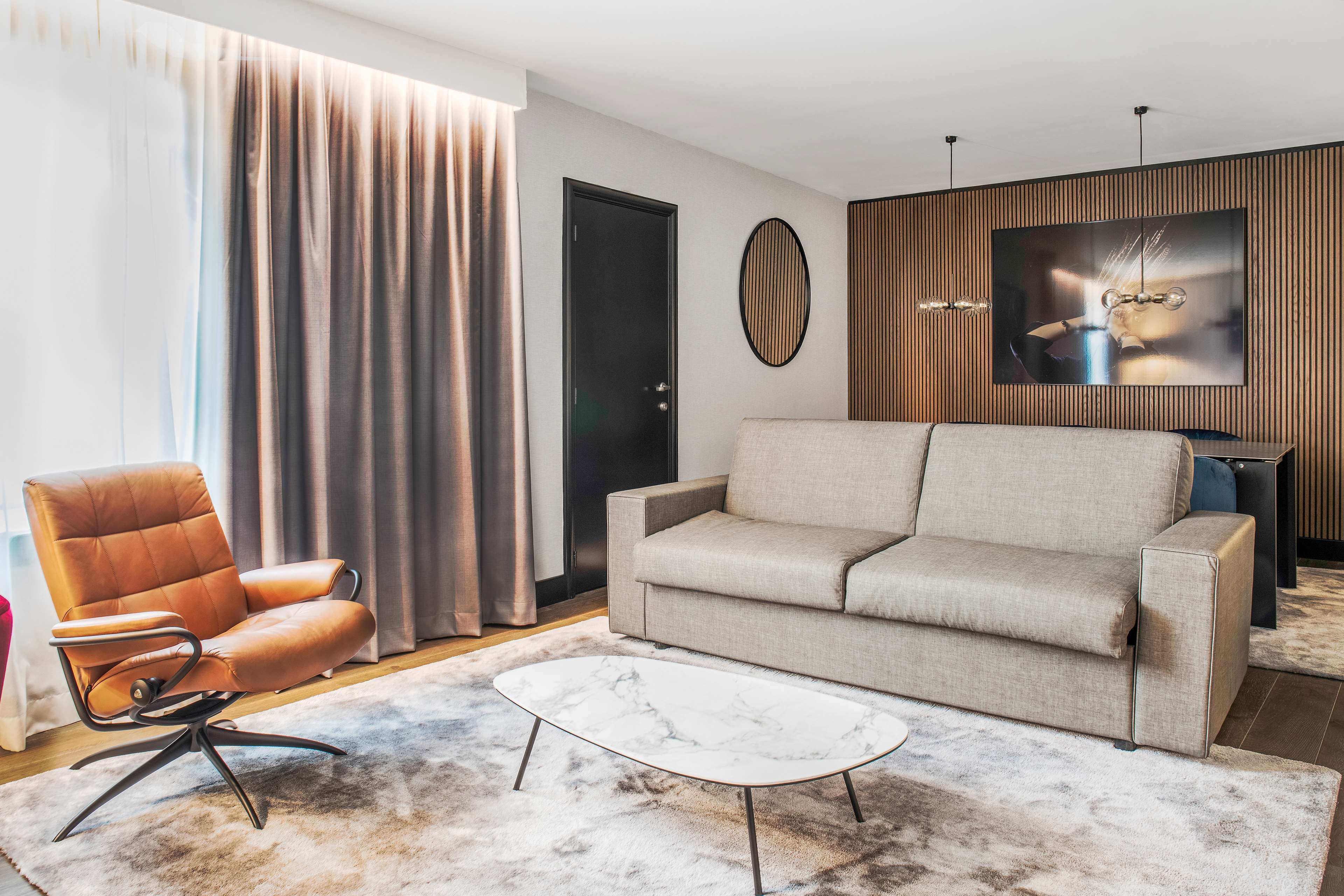 A modern living room with a leather armchair, a grey sofa, and a marble coffee table.