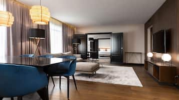 Habitación de hotel moderna con comedor, sofá, televisor y un ventanal con cortinas.