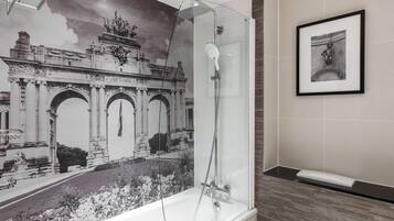 A bathroom with a glass-enclosed shower, a framed artwork on the wall, and a tiled floor.