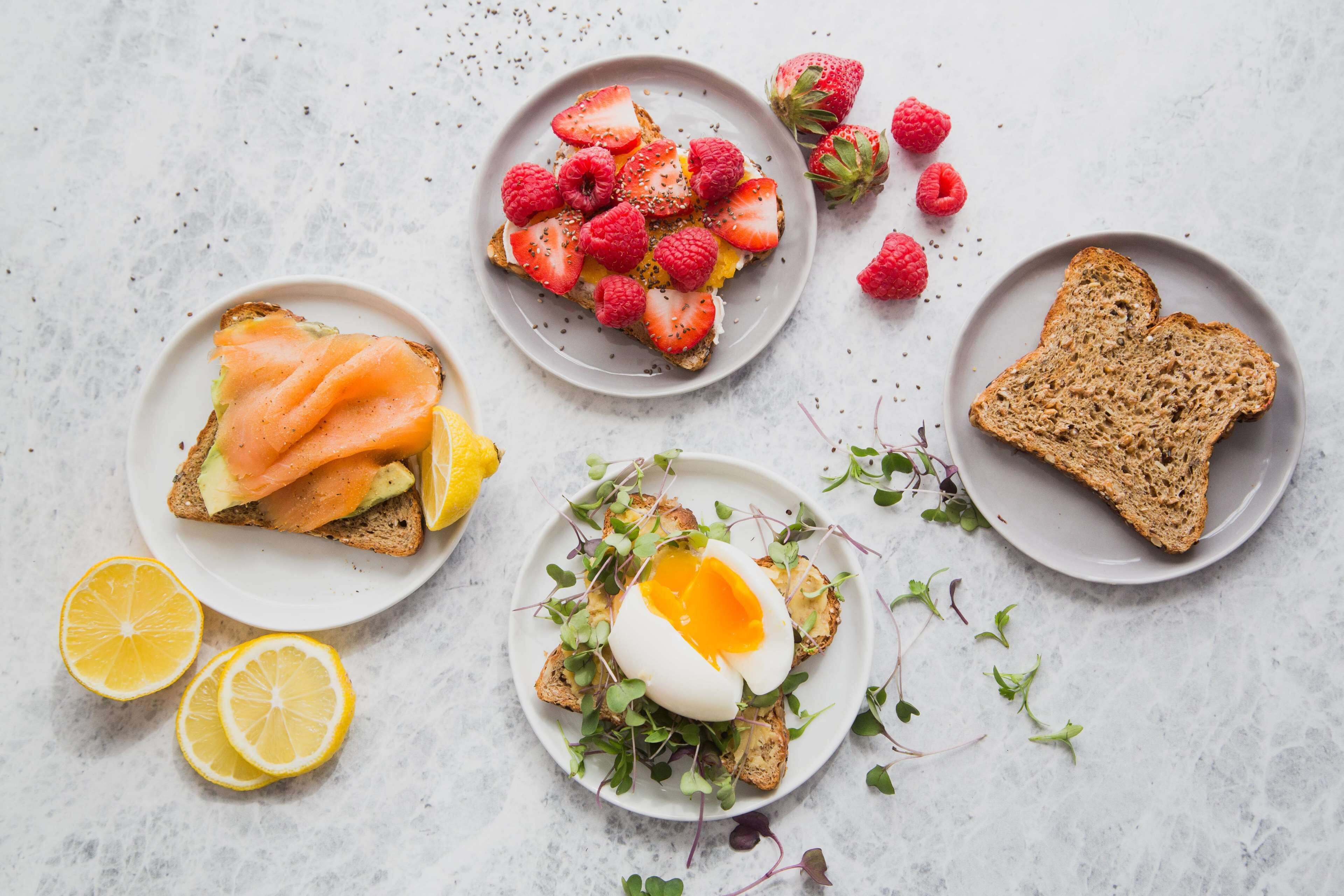 Diverse ontbijtartikelen, waaronder toast met zalm, aardbeien, frambozen en een gepocheerd ei, gepresenteerd op een bord met citroenpartjes.