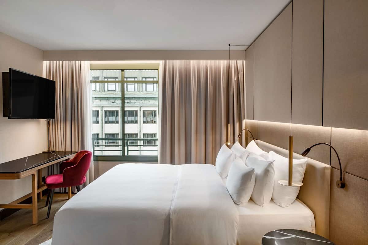 Une chambre d’hôtel avec un lit, un bureau et une chaise, une télévision et une fenêtre avec des rideaux.