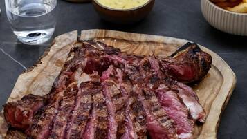 Een houten snijplank met plakjes steak, een saladeschaal en een glas water op een tafel.