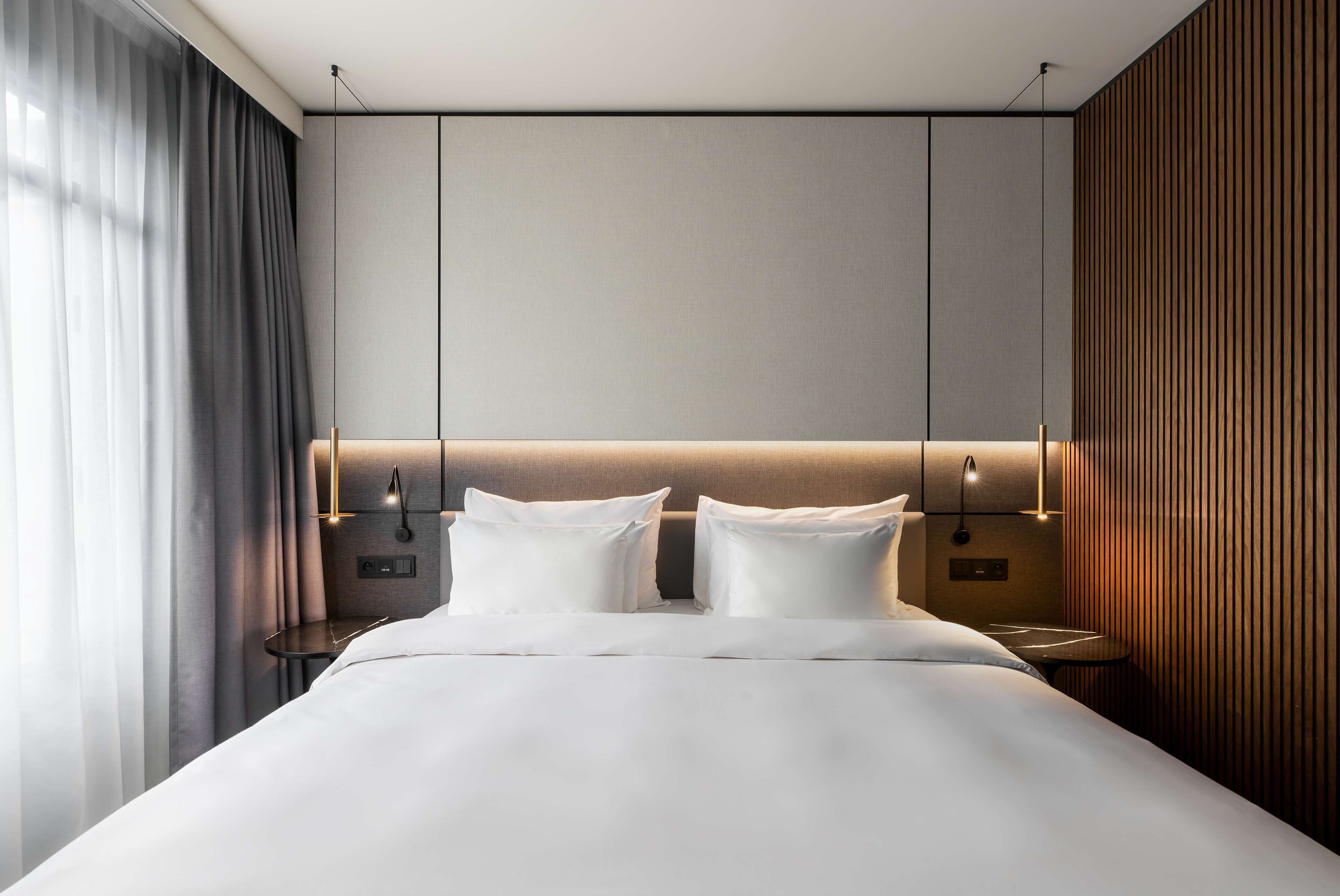 Une chambre d’hôtel moderne avec un grand lit, une table de chevet et un luminaire fixé au mur.